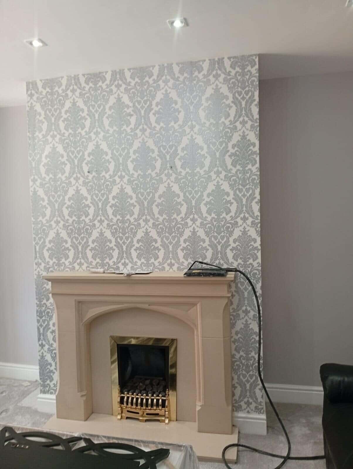 Before: chimney breast above a stone fireplace covered in grey patterned wallpaper