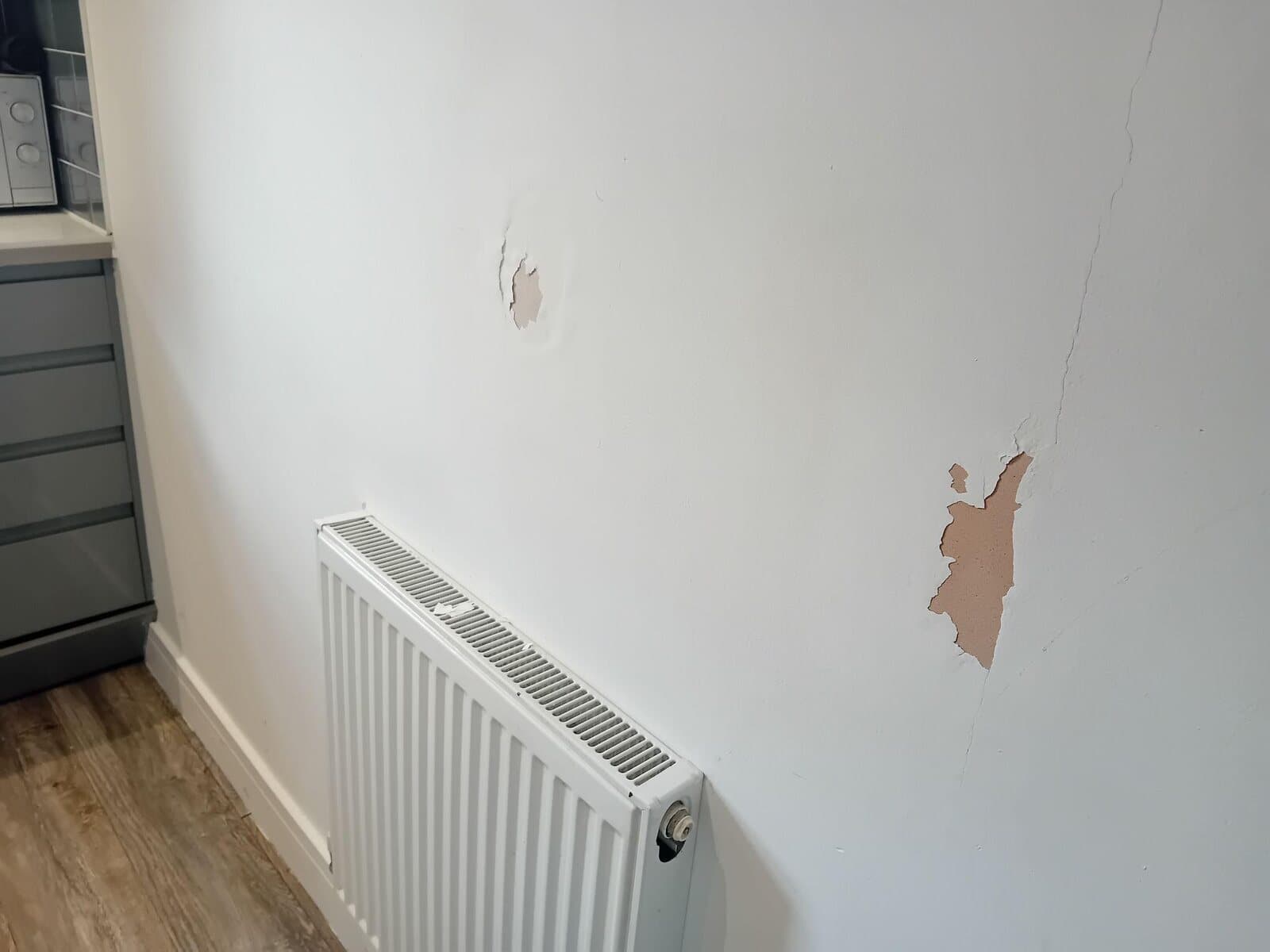 Before: wall beside a radiator with cracks and a patch of blown plaster