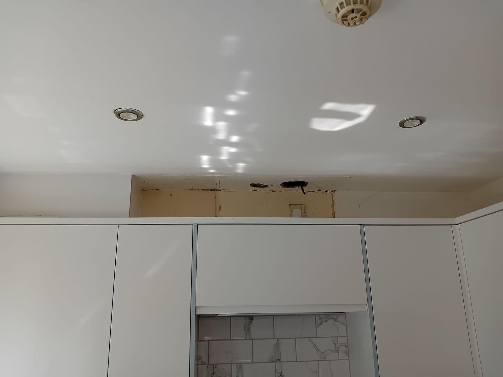 Before: kitchen ceiling with a dark stain and bare patch above white units
