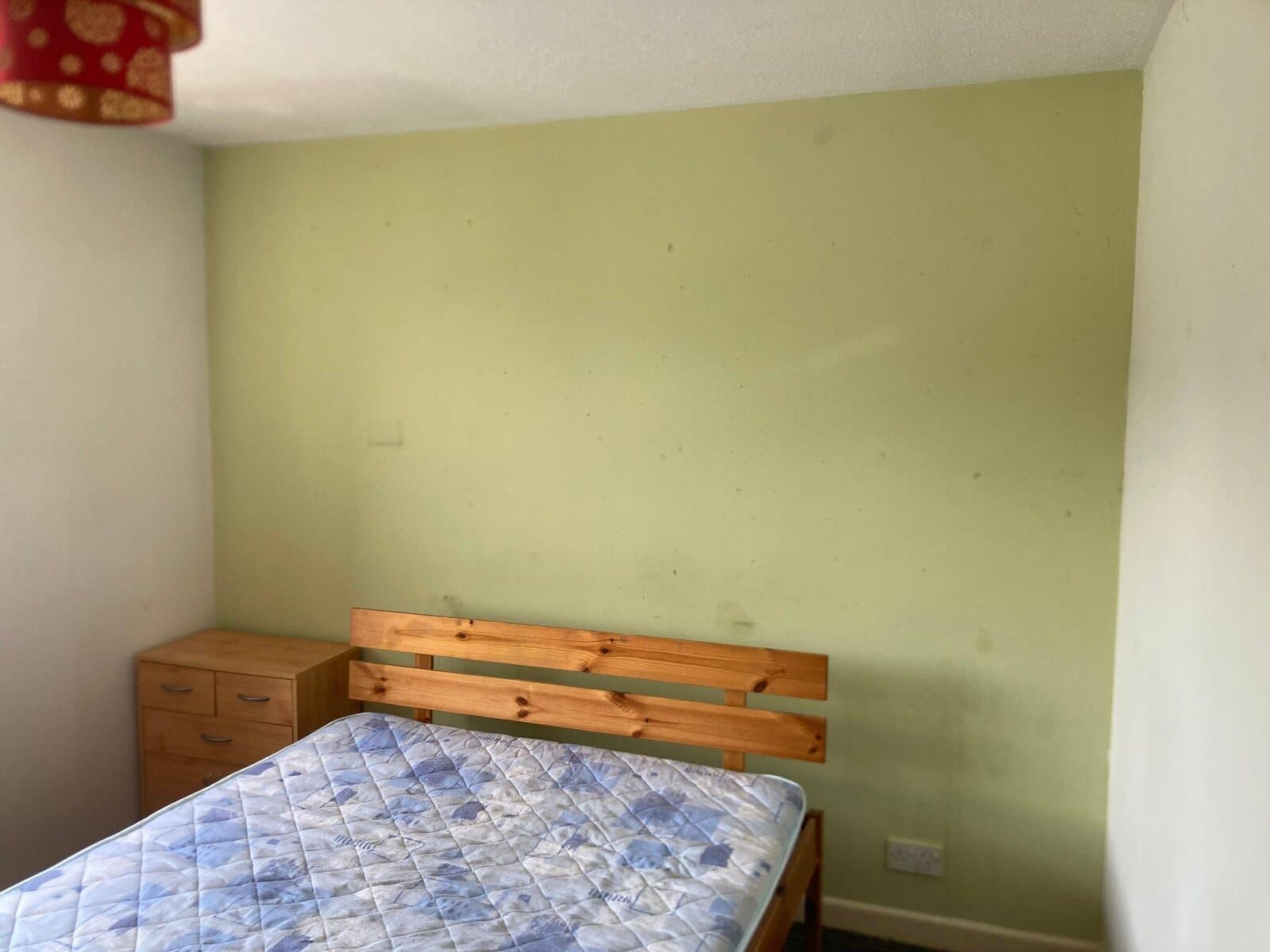 Before: bedroom with a pale green wall behind a pine bed
